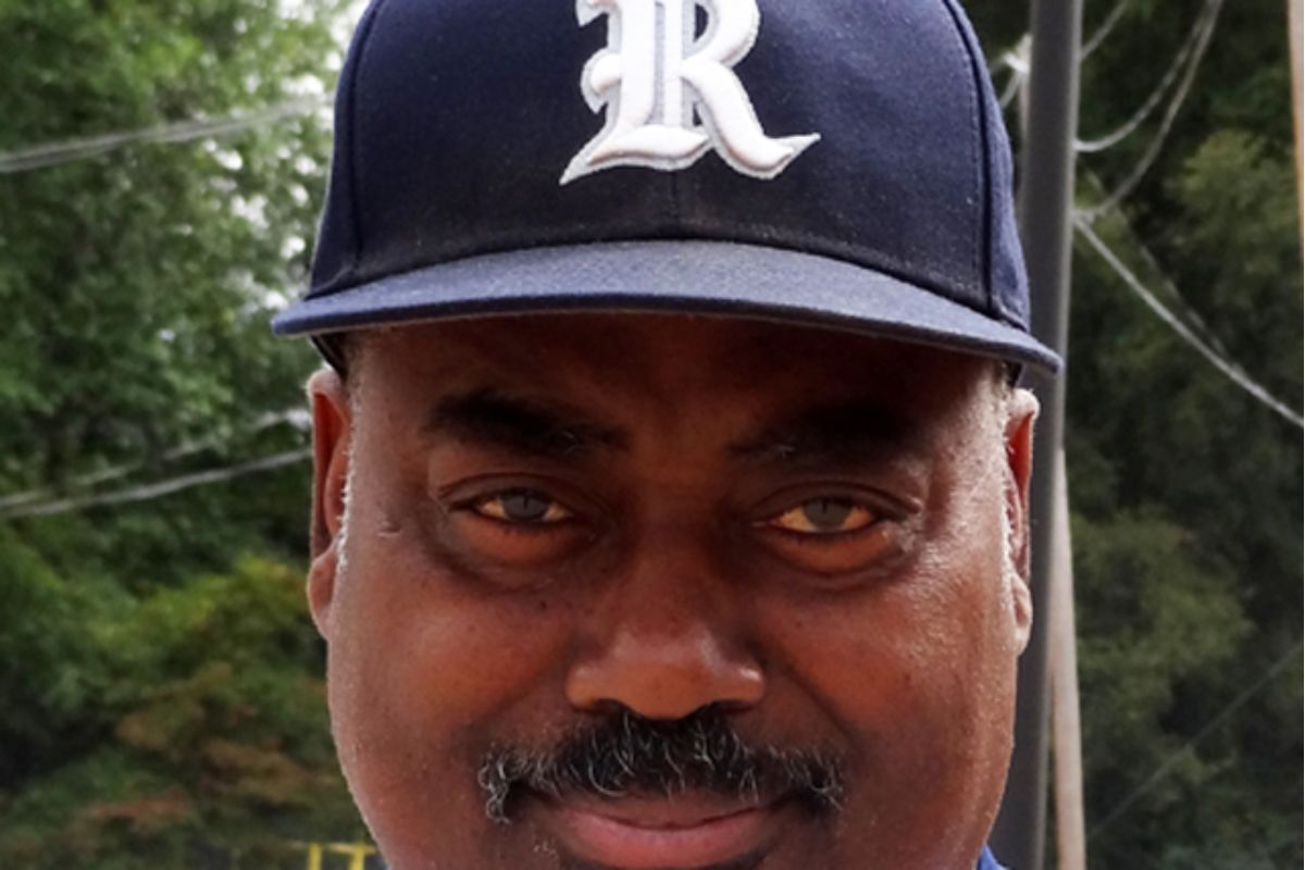 A man in a baseball cap and blue shirt stands confidently